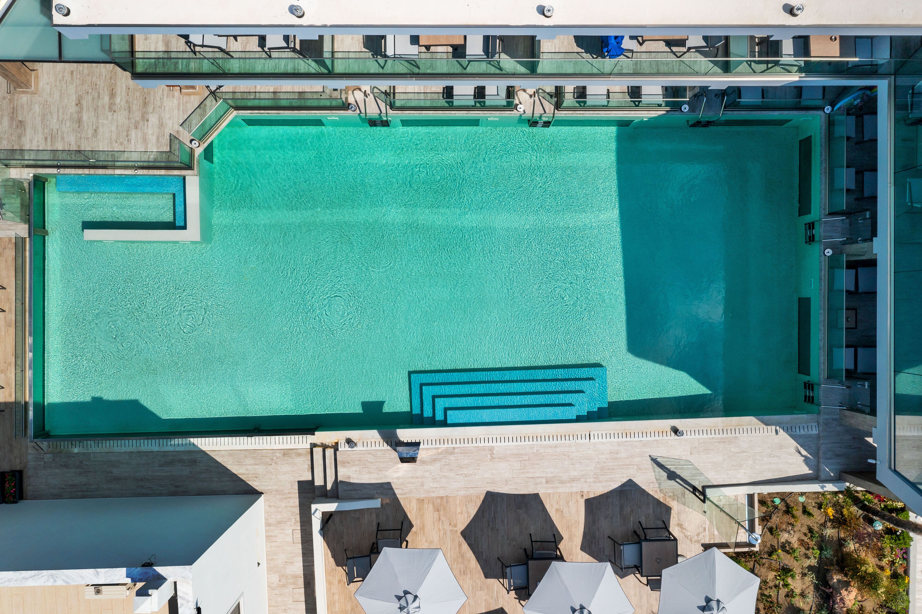 Luchtbeeld van een zwembad met een glazen balustrade, omringd door ligbedden en parasols.