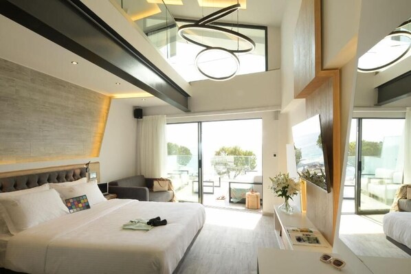 A modern hotel room with a large bed, a desk, and a balcony with outdoor furniture.