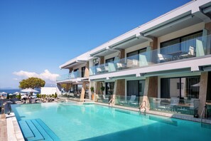 A modern hotel with a large pool, outdoor seating, and a view of the sea.