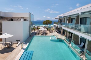 A rooftop pool with clear blue water, surrounded by lounge chairs and umbrellas, overlooking a beach and the sea.
