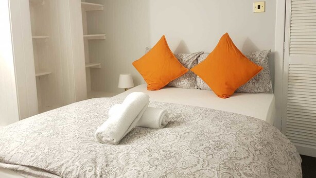 A neatly made bed with patterned bedding, two orange pillows, and a rolled white towel.