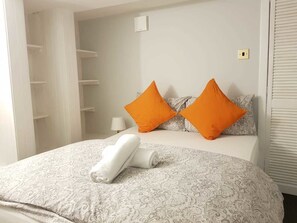 Een net opgemaakt bed met beddengoed met een patroon, twee oranje kussens en een opgerolde witte handdoek.