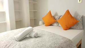A neatly made bed with rolled white towels, two orange pillows, and a patterned bedspread.