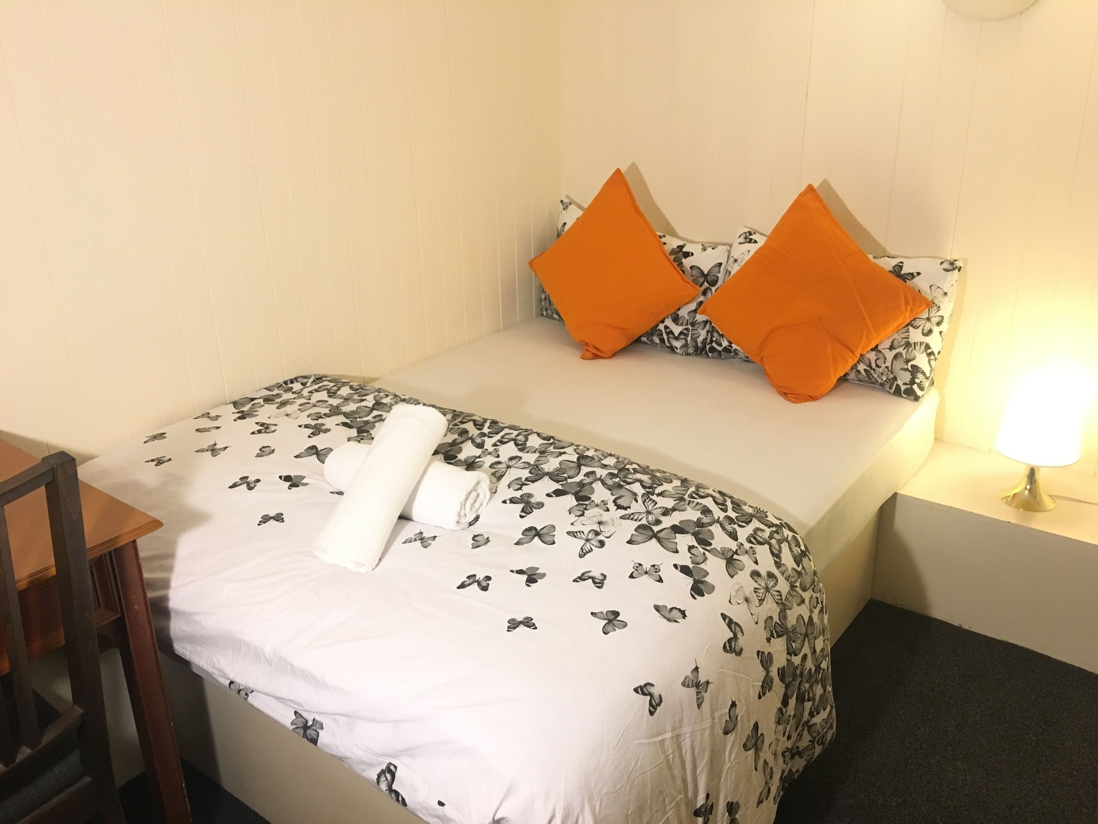 A neatly made bed with a floral bedspread, two orange pillows, and a rolled white towel.