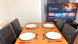 A dining table set with white plates, red-handled cutlery, and a television displaying a music video. - The Dalgety Apartments (Edinburgh)