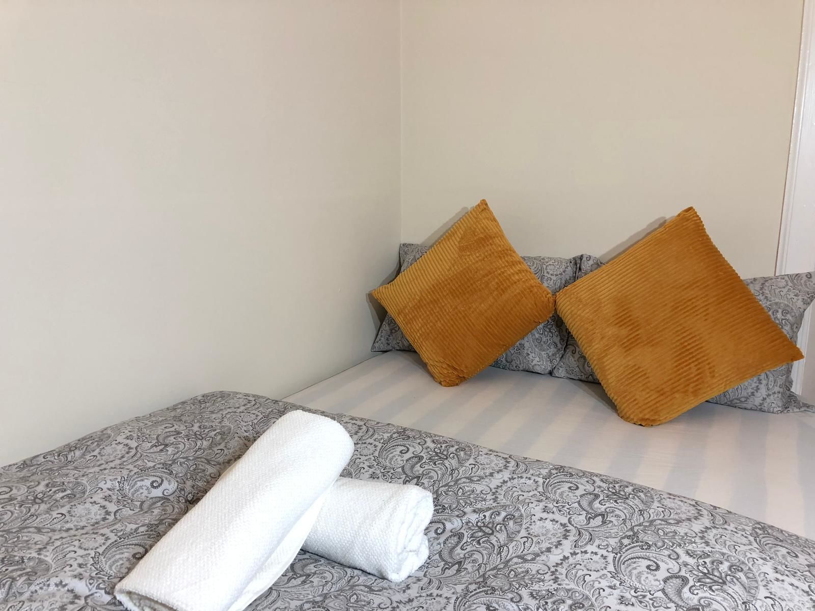 A neatly made bed with patterned bedding and two pillows, one in a light color and the other in a mustard shade.