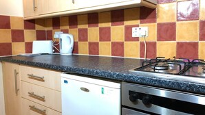 A compact kitchen with a gas stove, a built-in oven, a dishwasher, and wooden cabinets. - The Dalgety Apartments (Edinburgh)