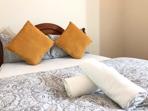 Un lit avec une couvre-lit à motifs, deux oreillers et une couverture pliée.