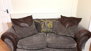 A gray sofa with two brown leather armrests and a decorative pillow with a leaf pattern. - The Dalgety Apartments (Edinburgh)