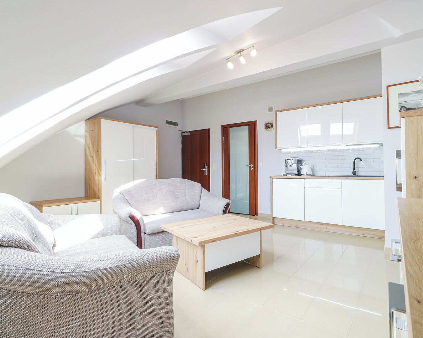A modern loft apartment with a dining area, kitchenette, and a large window providing natural light.