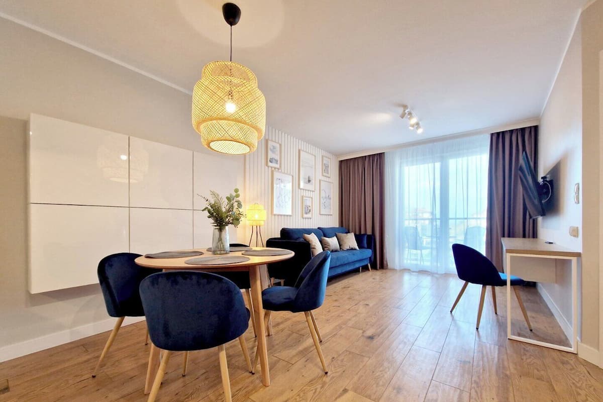 A modern living room with a round dining table, blue chairs, a sofa, and a TV on a stand.