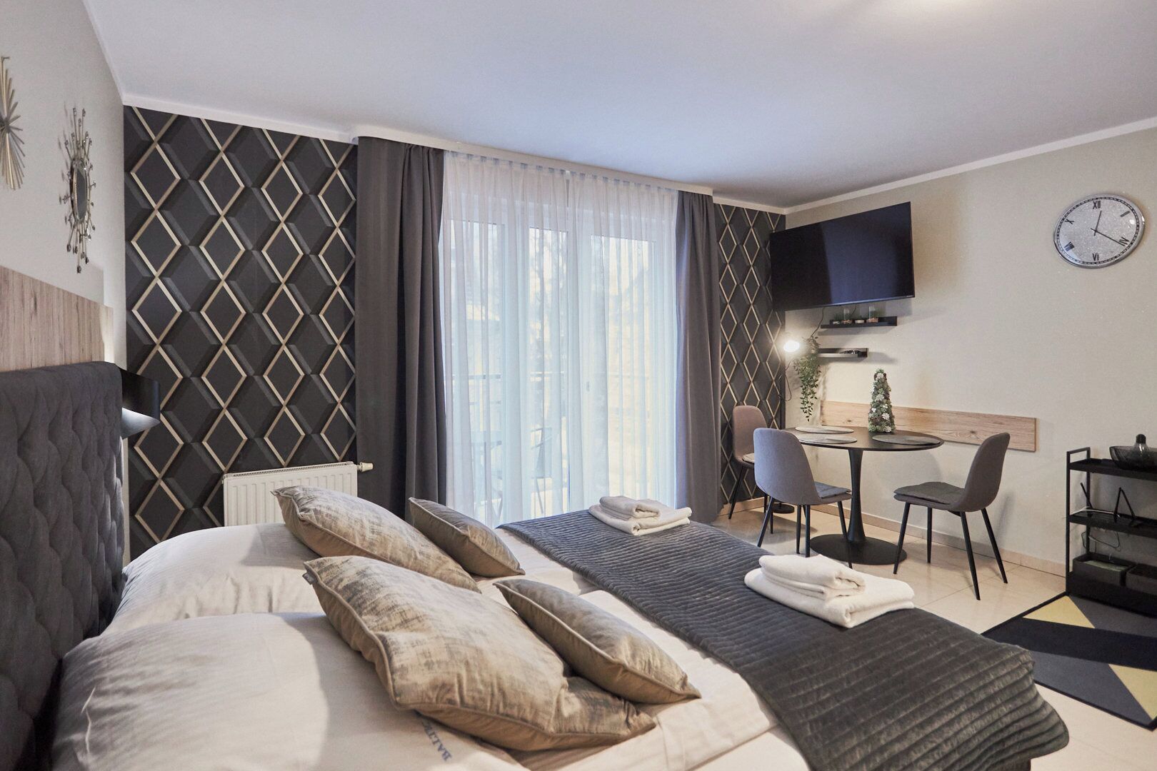 Habitación de hotel con cama, escritorio, silla, televisión y reloj en la pared.