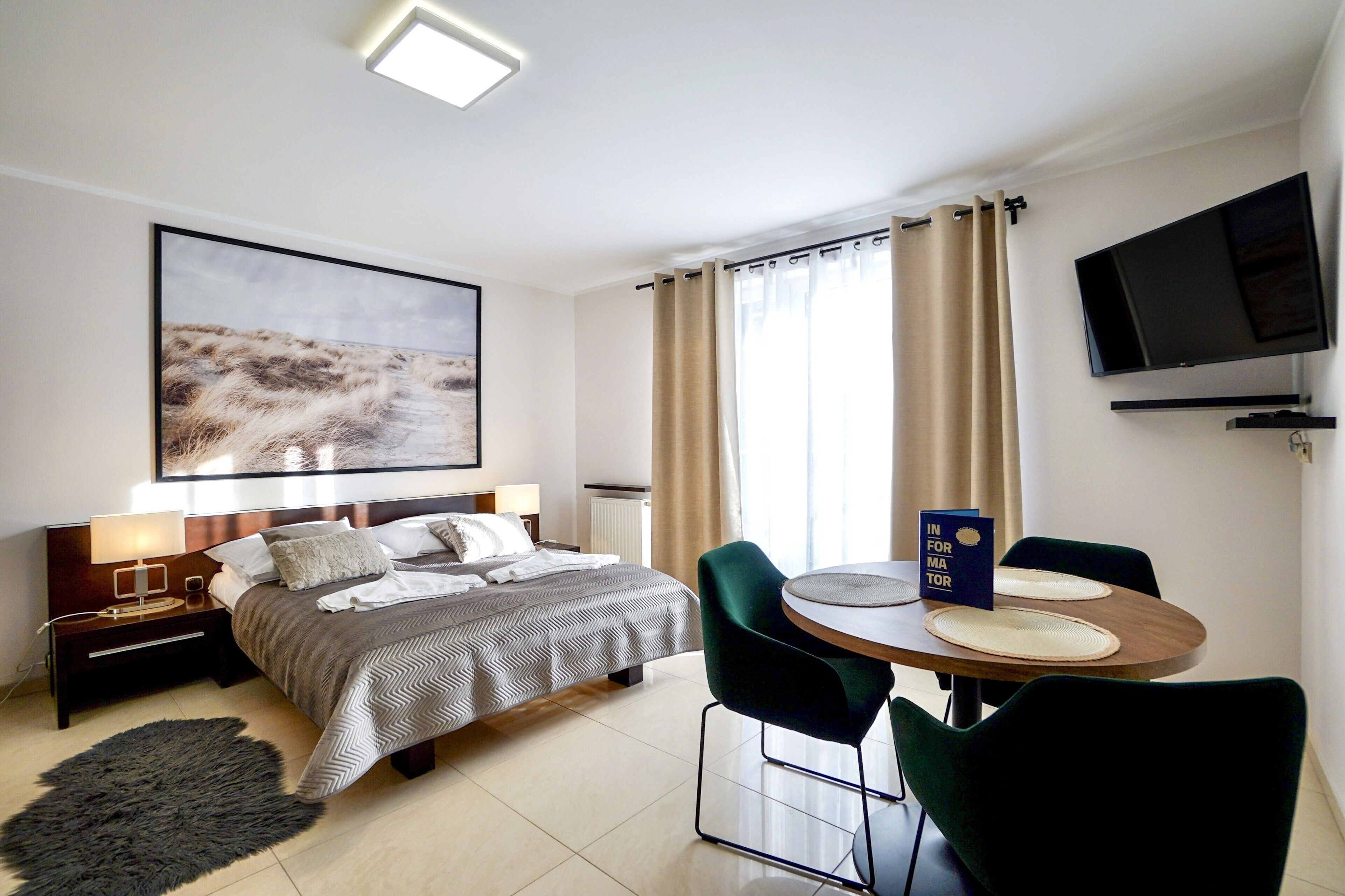 A hotel room with a bed, bedside table, lamp, TV, and a dining area with chairs and a table.