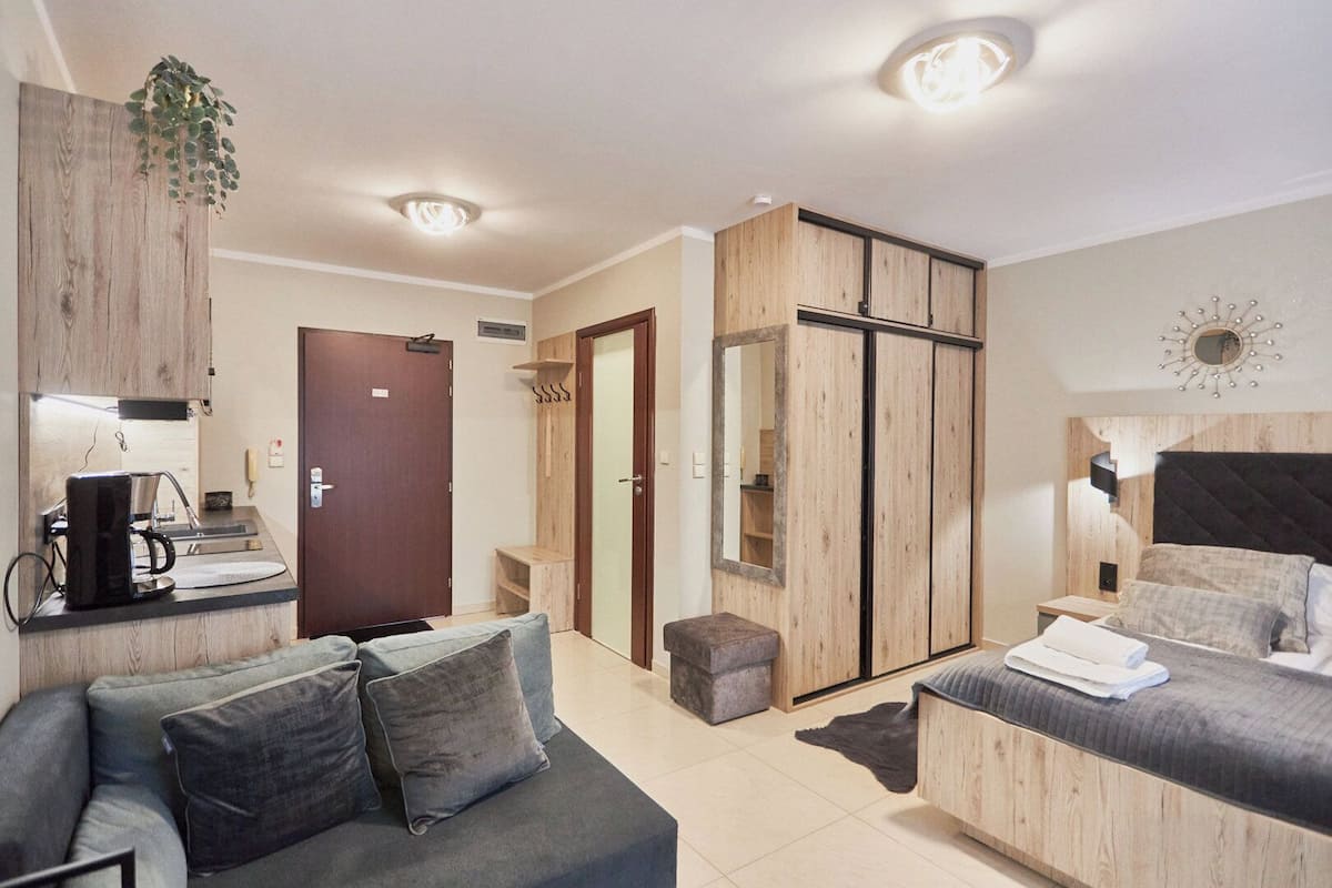 A modern hotel room with a sofa, a bed, a wooden wardrobe, a mirror, and a coffee machine.