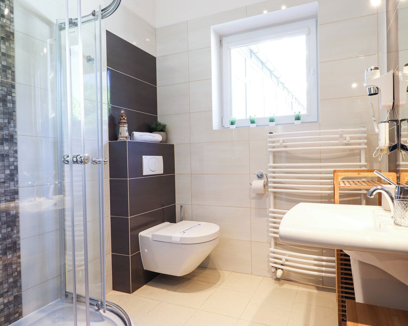 A modern bathroom with a glass shower enclosure, a toilet, a sink with a mirror, and a window providing natural light.