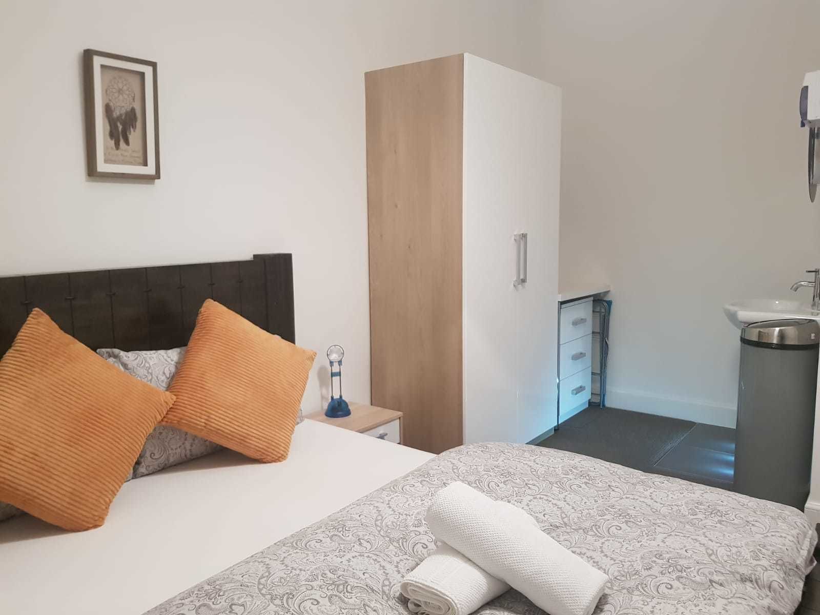 A hotel room with a bed, a wardrobe, a bedside table, a sink, and a mirror.