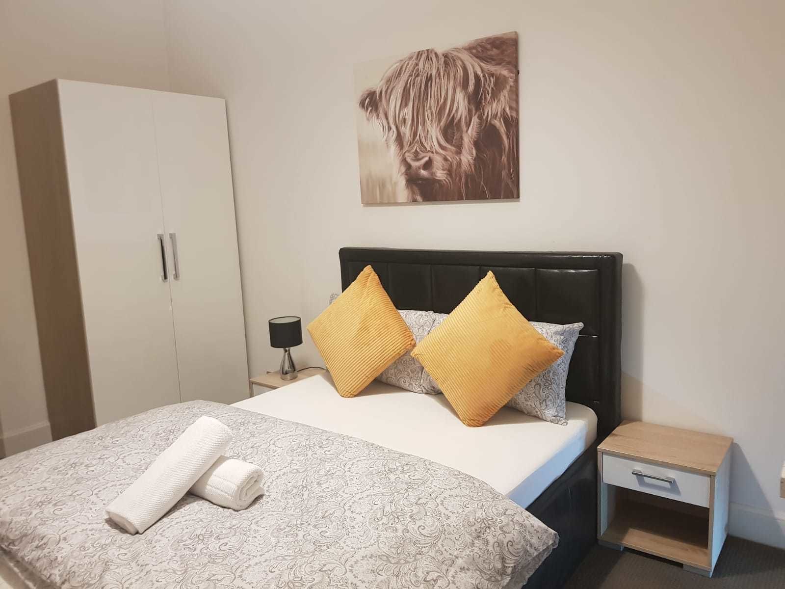 A bedroom with a bed, a nightstand, a wardrobe, and a wall-mounted artwork.