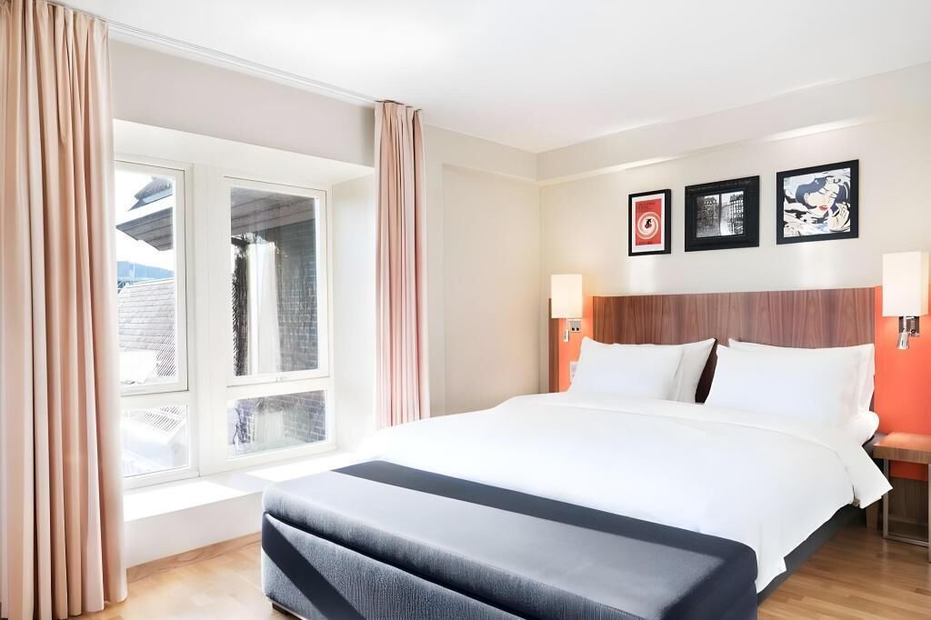 A hotel room with a large bed, a window with curtains, a wooden headboard, and three framed pictures on the wall.