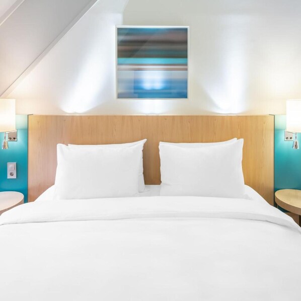 Quarto de hotel com uma cama grande, duas mesas de cabeceira e uma obra de arte moderna na parede.