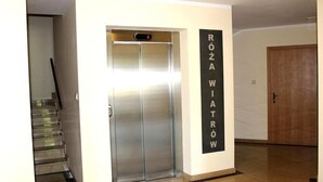 A modern elevator with a digital display showing the number 4. Adjacent to the elevator is a wall-mounted sign with the text "ROZA WIATROW". - Rosa Weneda by Baltic Home (Swinoujscie)
