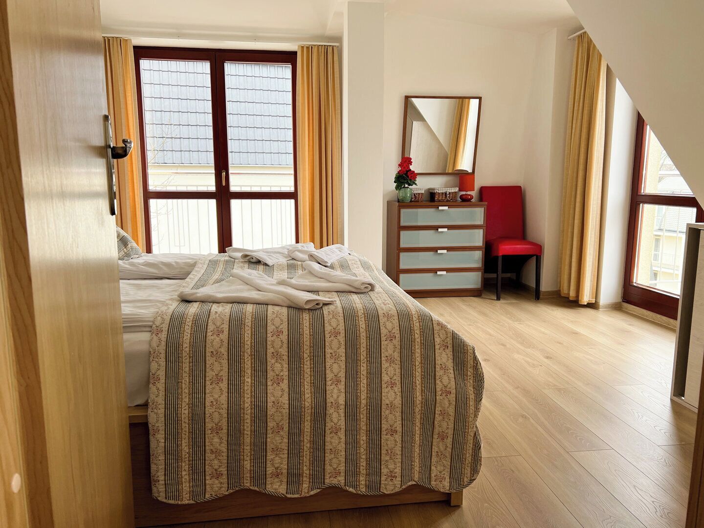 Um quarto com uma cama, cômoda, cadeira e espelho.
