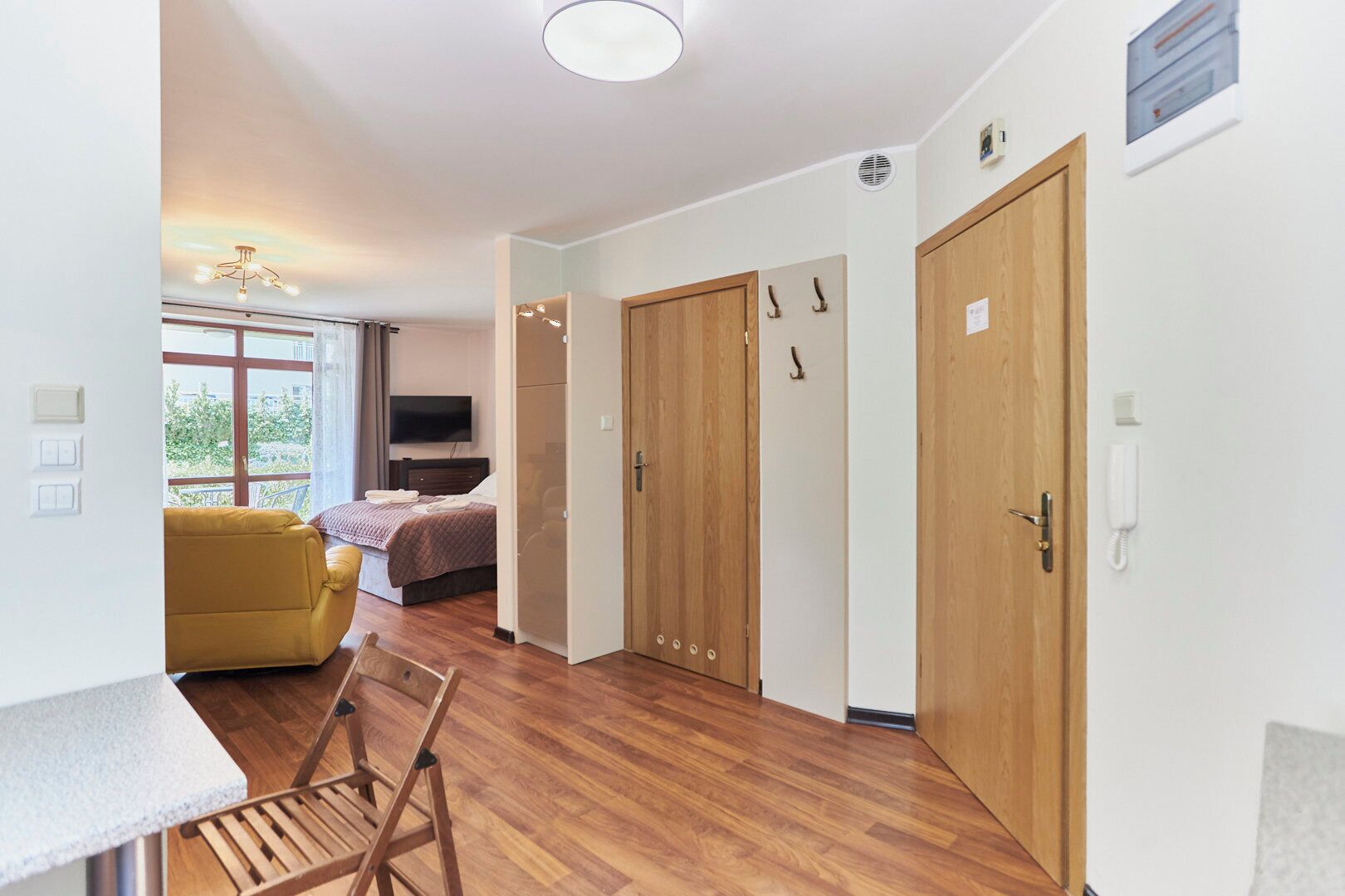 Una habitación moderna con suelo de madera, un sofá amarillo, una cama con televisor y un armario de madera.