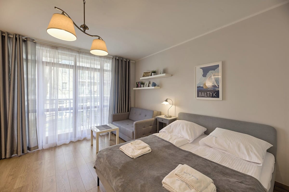 Een hotelkamer met een bed, nachtkastje, lamp en uitzicht buiten door grote ramen.