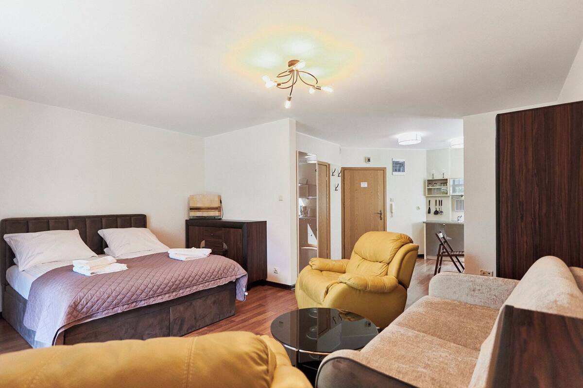 Een hotelkamer met een bed, een stoel, een bank, een tafeltje en een kitchenette op de achtergrond.