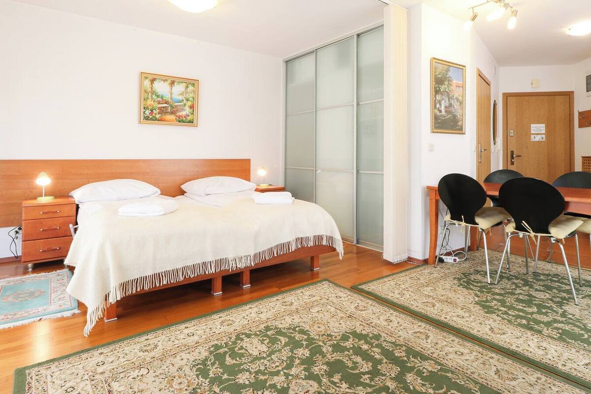 Een hotelkamer met een bed, nachtkastjes, een bureau met stoelen, een groot raam en een deur.