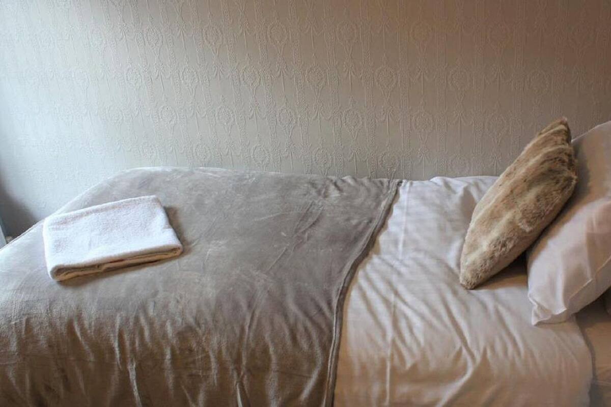 A bed with a folded white towel and a single pillow.