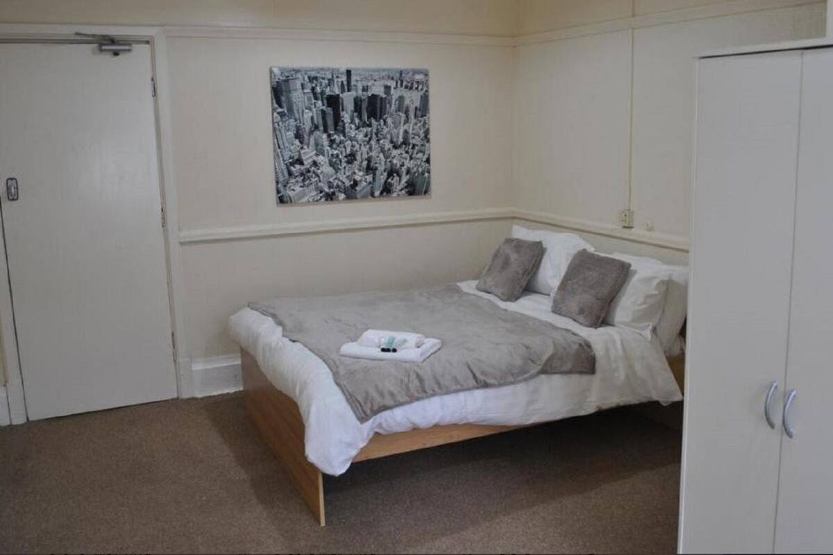 A bedroom with a bed, a wardrobe, and a black and white cityscape painting on the wall.