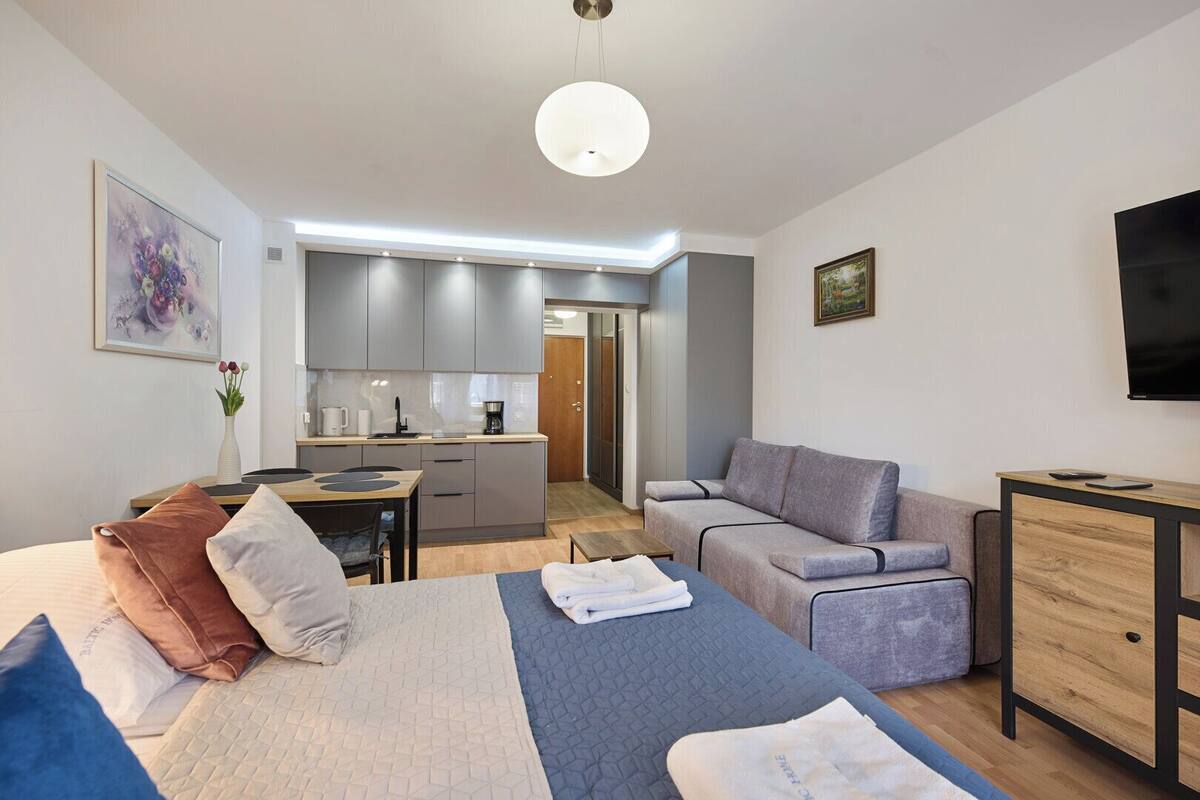 A modern hotel room with a bed, a sofa, a desk, and a kitchenette.