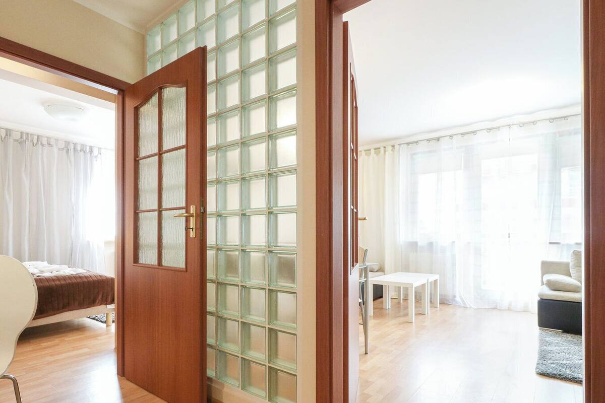 A spacious living area with a wooden floor, a glass partition wall, a white sofa, a small round table, and a chair.