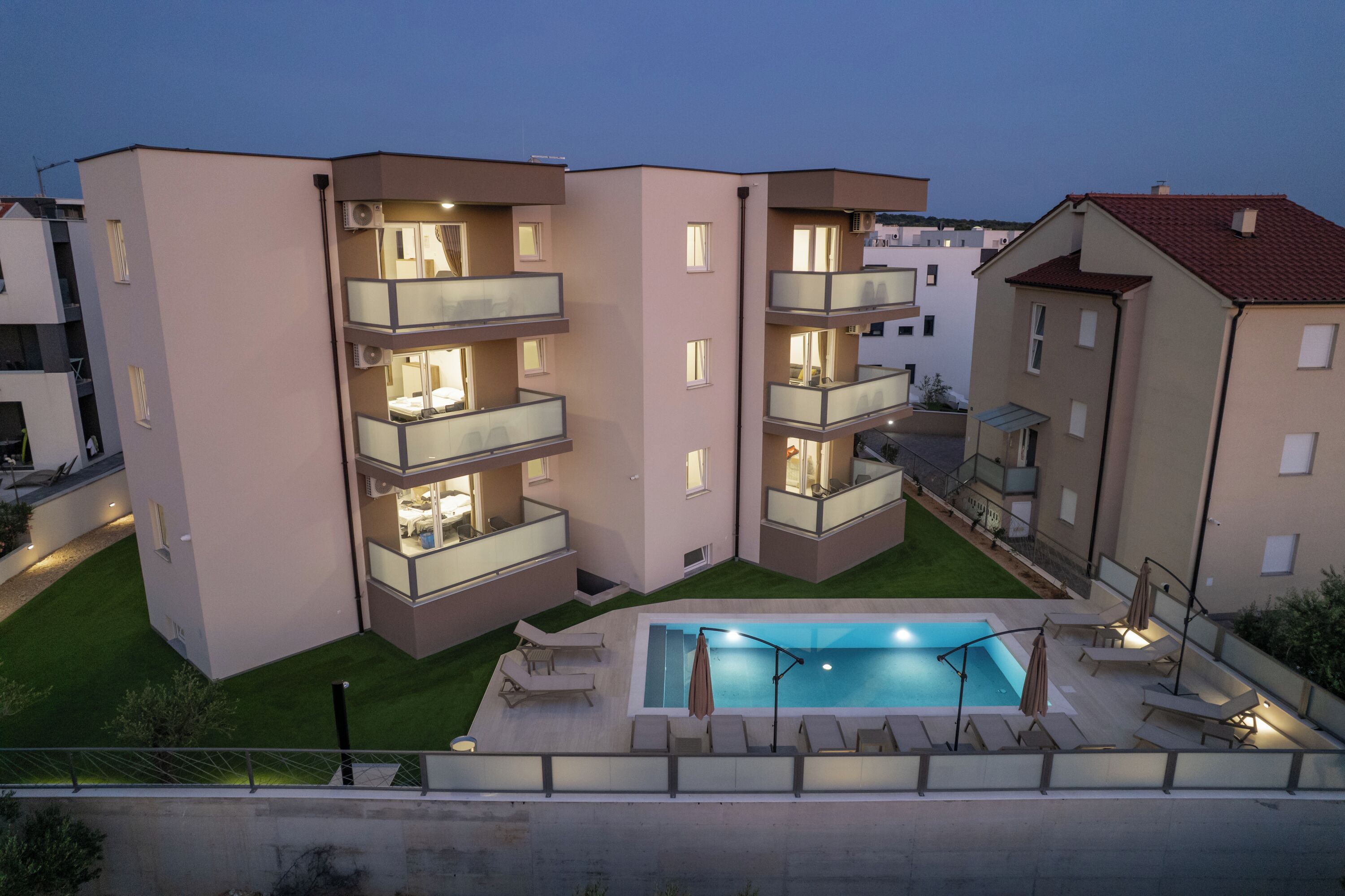 A modern apartment building with a swimming pool, multiple balconies, and outdoor seating.