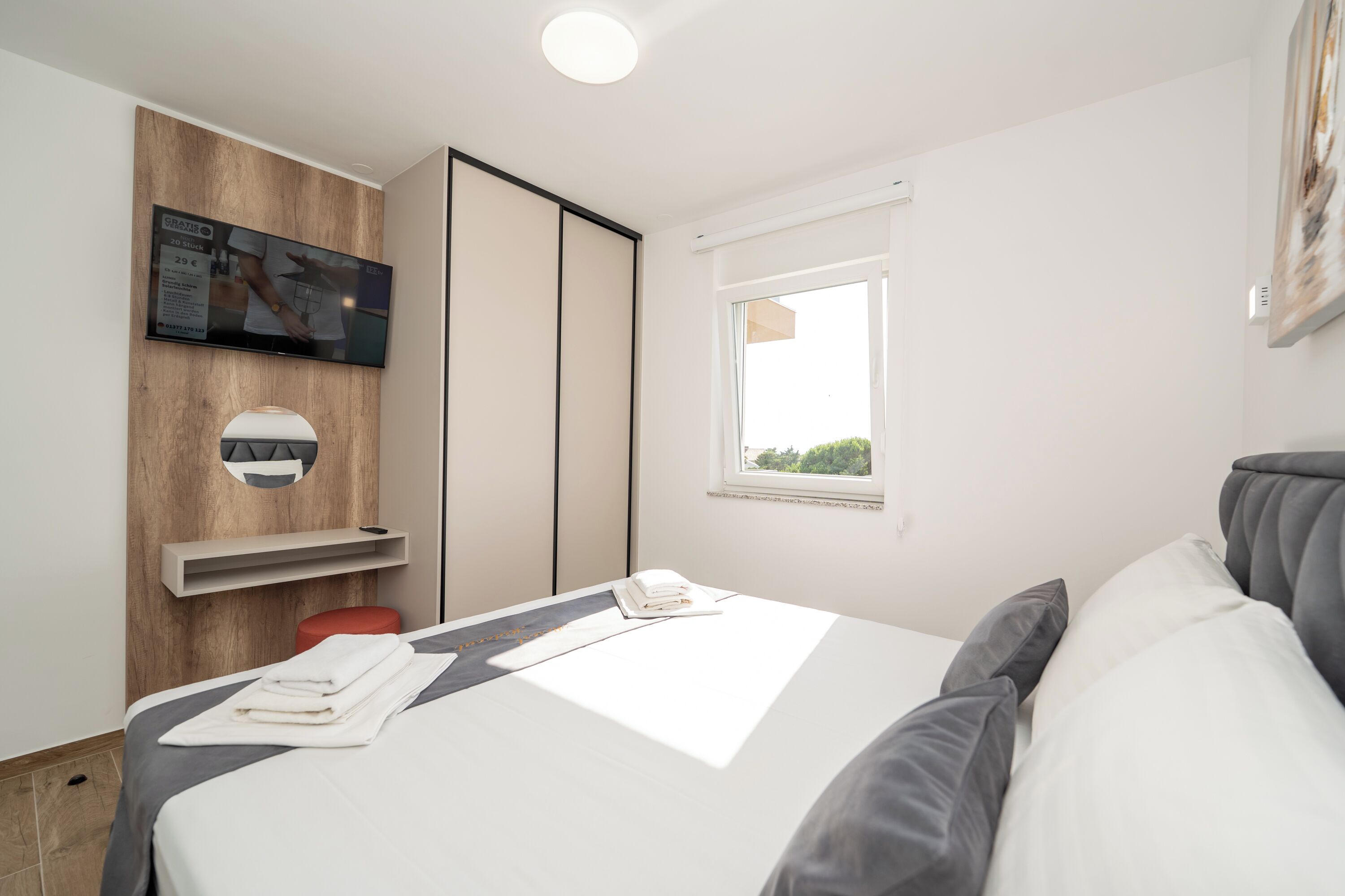 Una moderna camera d'hotel con un letto, una TV fissata a un pannello di legno, una finestra e vista sul verde.
