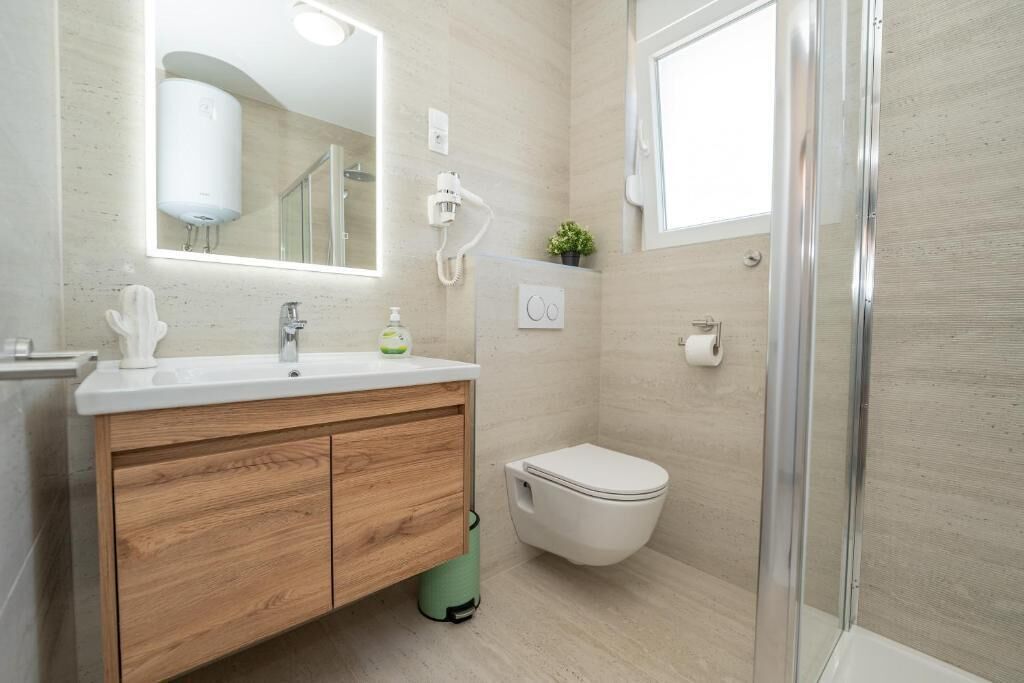 Un bany modern amb un moble de tocador de fusta, un vàter, una cabina de dutxa i un mirall.