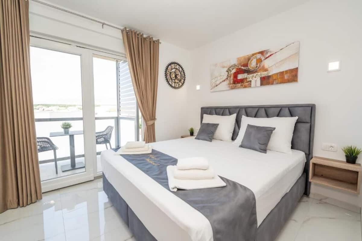 Une chambre d’hôtel moderne dotée d’un grand lit, d’un balcon avec une table et des chaises, et offrant une vue sur la plage.