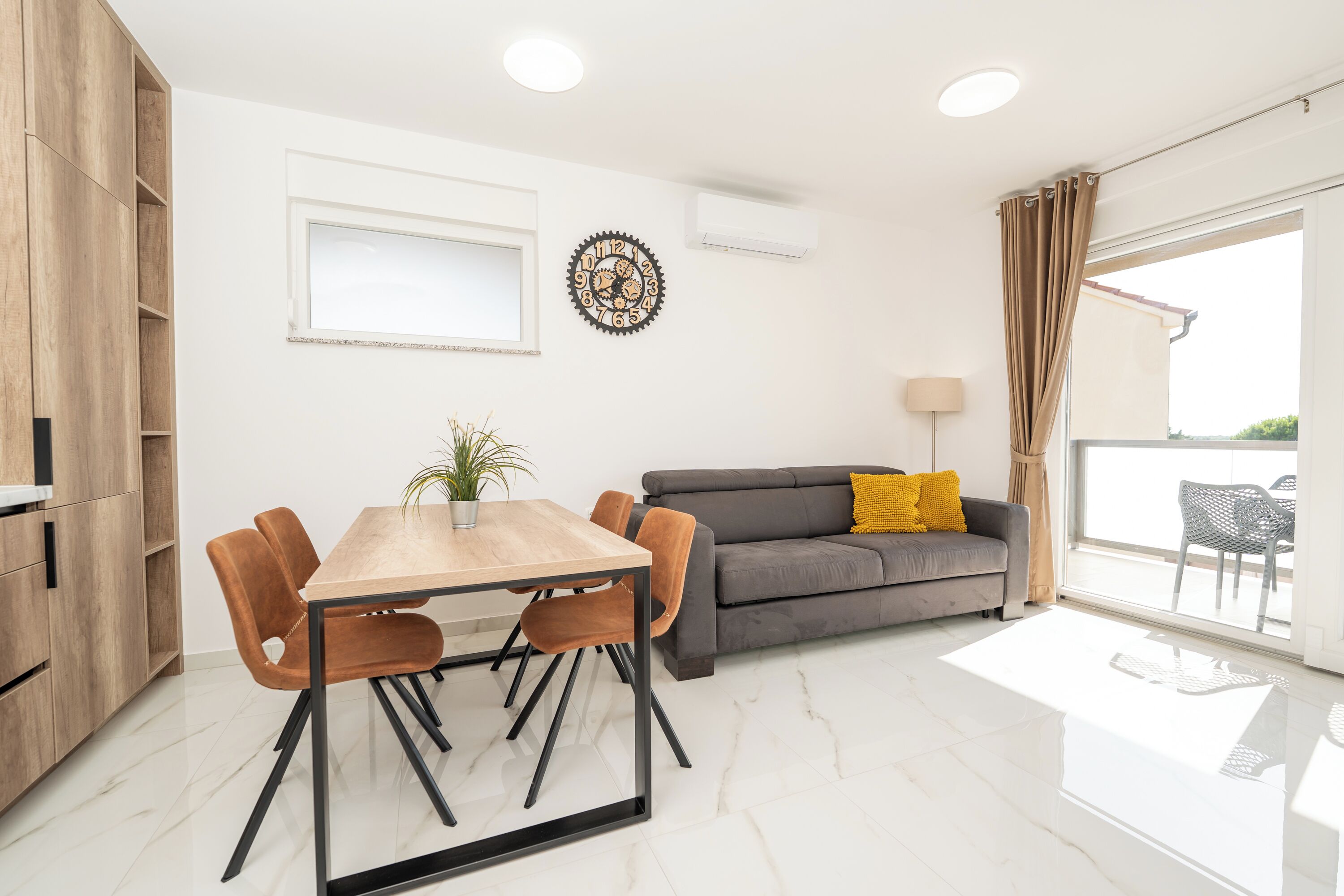 A modern living room with a dining area, a grey sofa with yellow cushions, a wooden cabinet, and a large window with curtains.