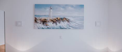 A bedroom with a large bed, two bedside lamps, and a painting of a lighthouse on the wall.