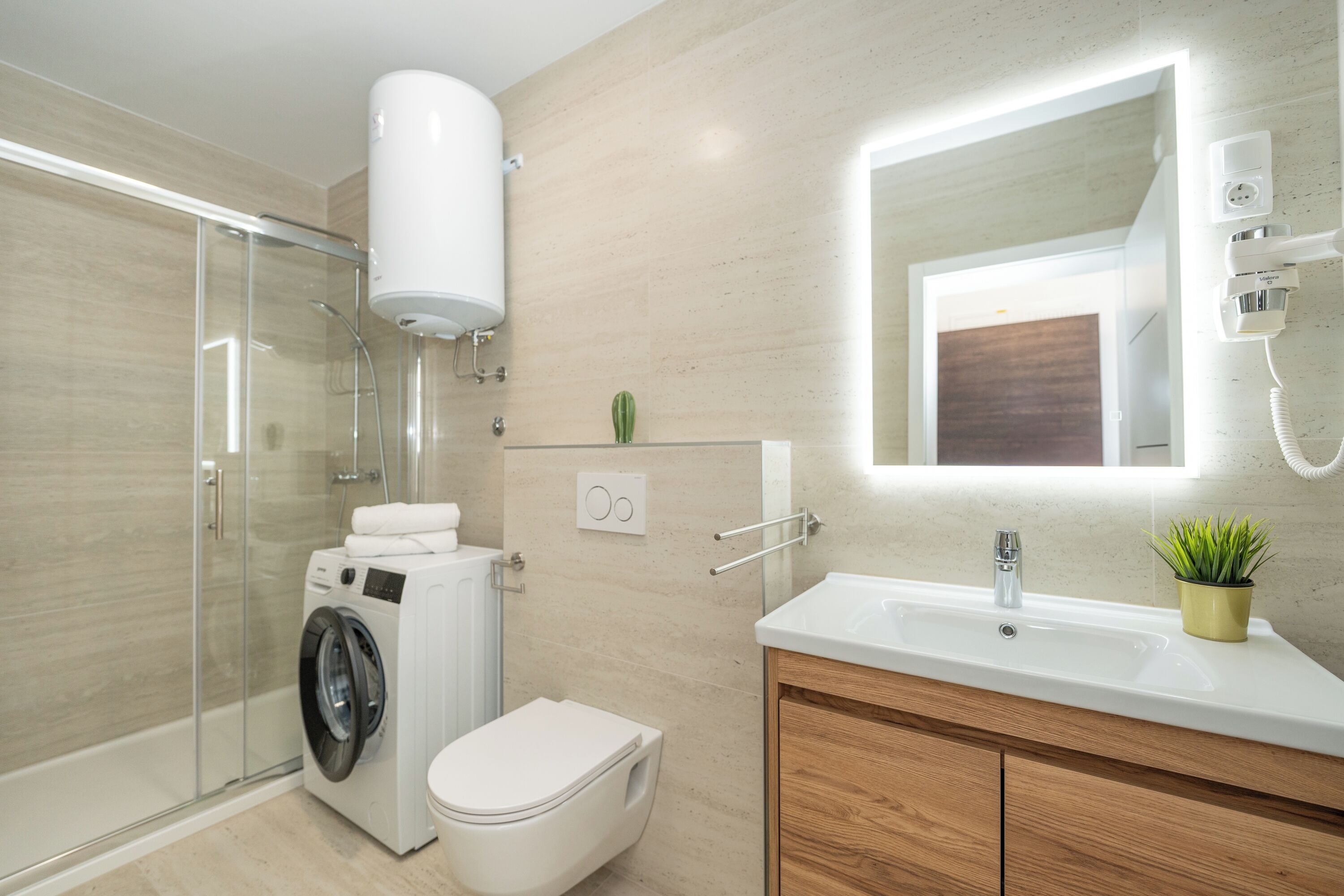 Un baño moderno con cabina de ducha de vidrio, lavadora integrada, inodoro y tocador con lavabo y espejo.