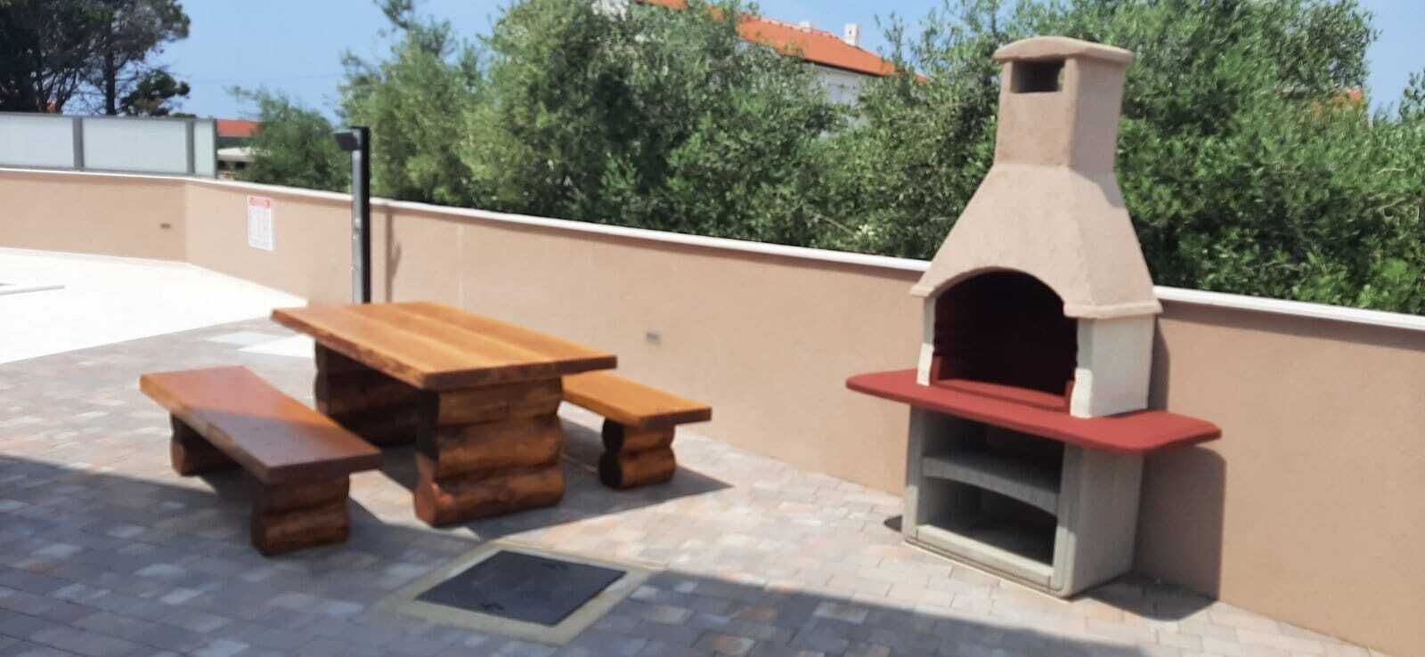 An outdoor patio with a wooden table and benches, and a brick oven.