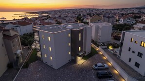 A modern residential area with a clear view of the sunset over the water, featuring contemporary buildings with flat roofs and a parking area with several cars. - Poolside Hideout Apartments (Novalja)