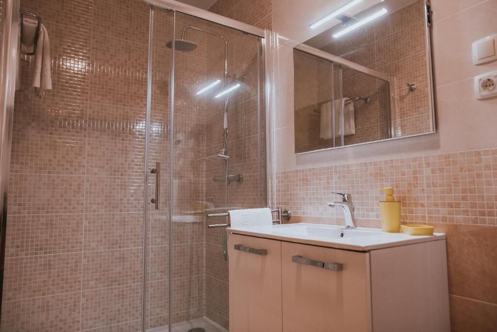A bathroom with a glass-enclosed shower, a sink with a mirror above it, and a cabinet with toiletries.