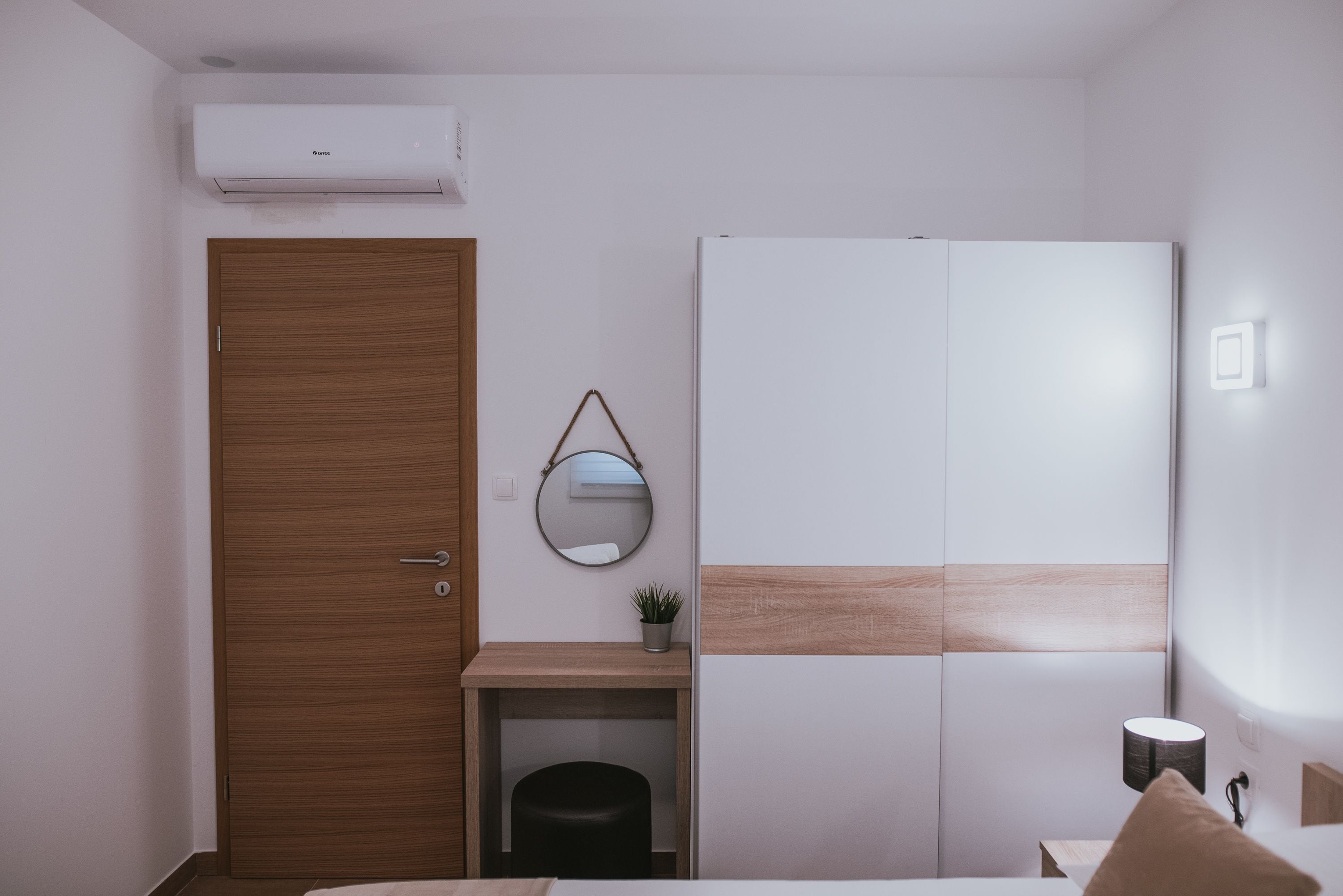 Una camera da letto con una porta in legno, un comodino con una lampada, un armadio e uno specchio a parete.