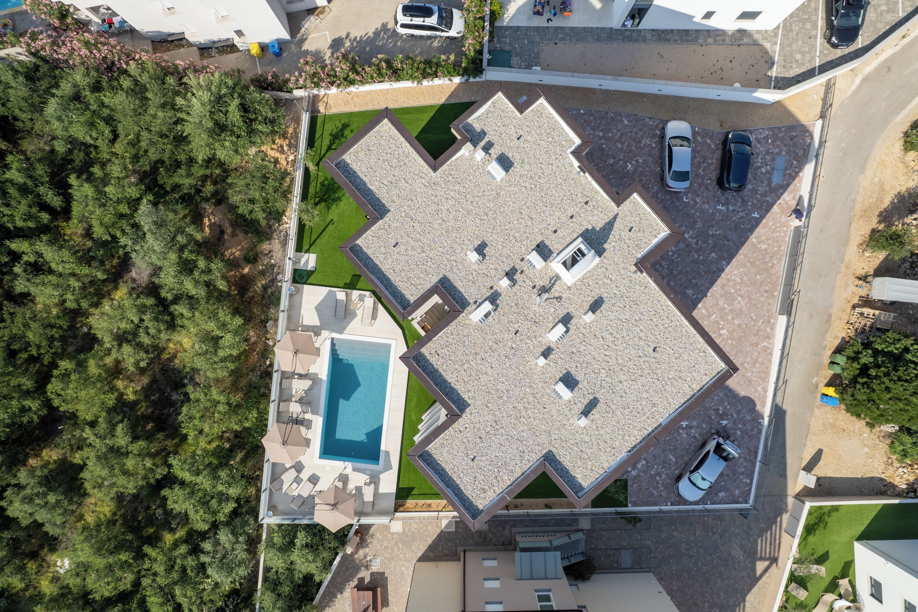 An aerial view of a property with a swimming pool, multiple parking spaces, and a landscaped garden.
