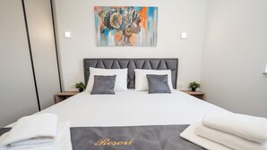 A hotel room with a large bed, two bedside tables, a painting on the wall, and a sign on the bedspread reading "Resort Hideout". - Poolside Hideout Apartments (Novalja)