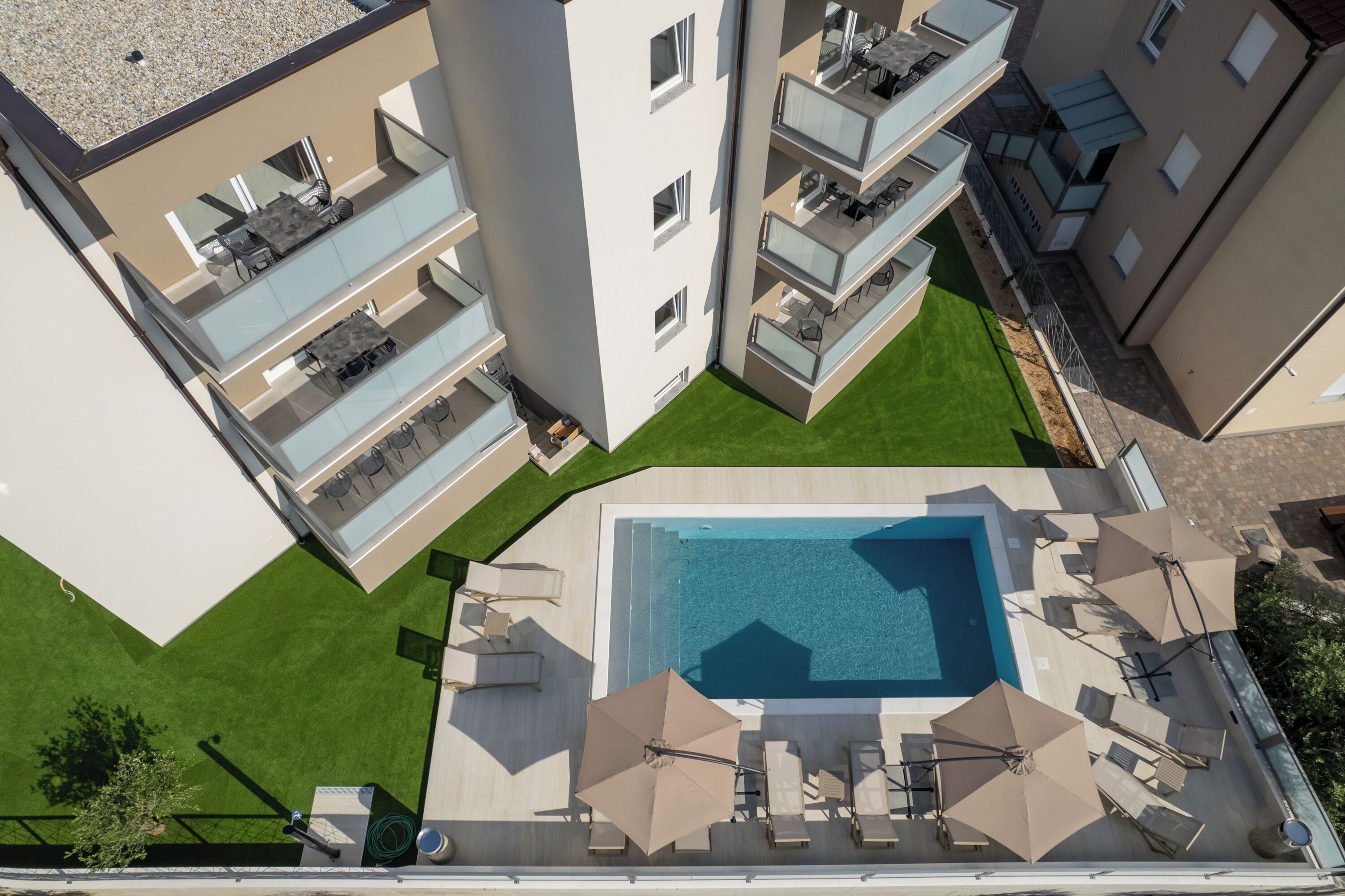 Vista aèria d'un edifici d'apartaments modern amb una piscina central, nombrosos balcons i zones d'estar a l'aire lliure.