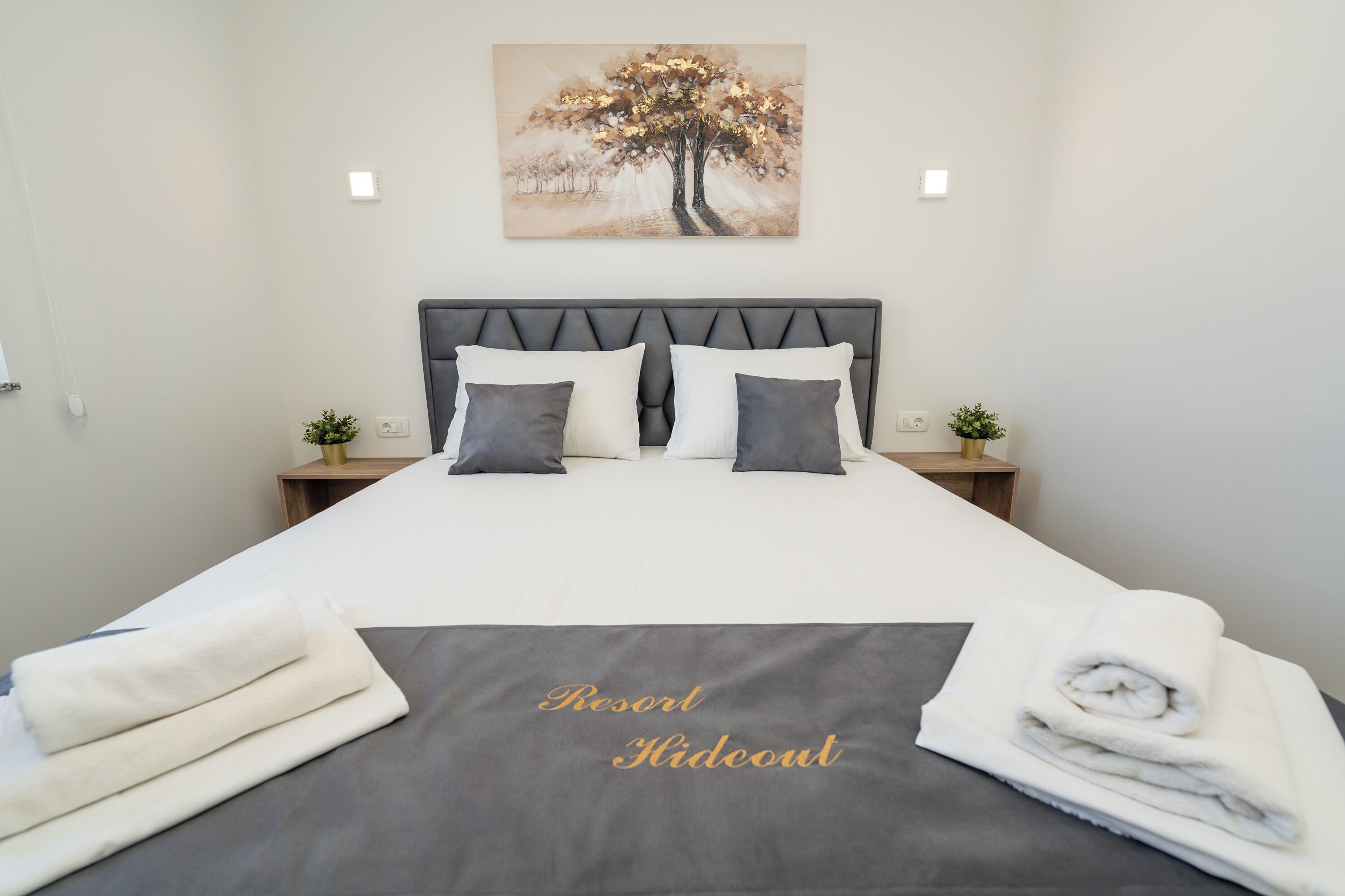 Un lit bien fait, avec une tête de lit grise, une literie blanche et un plaid gris orné du texte « Resort Hideout ».