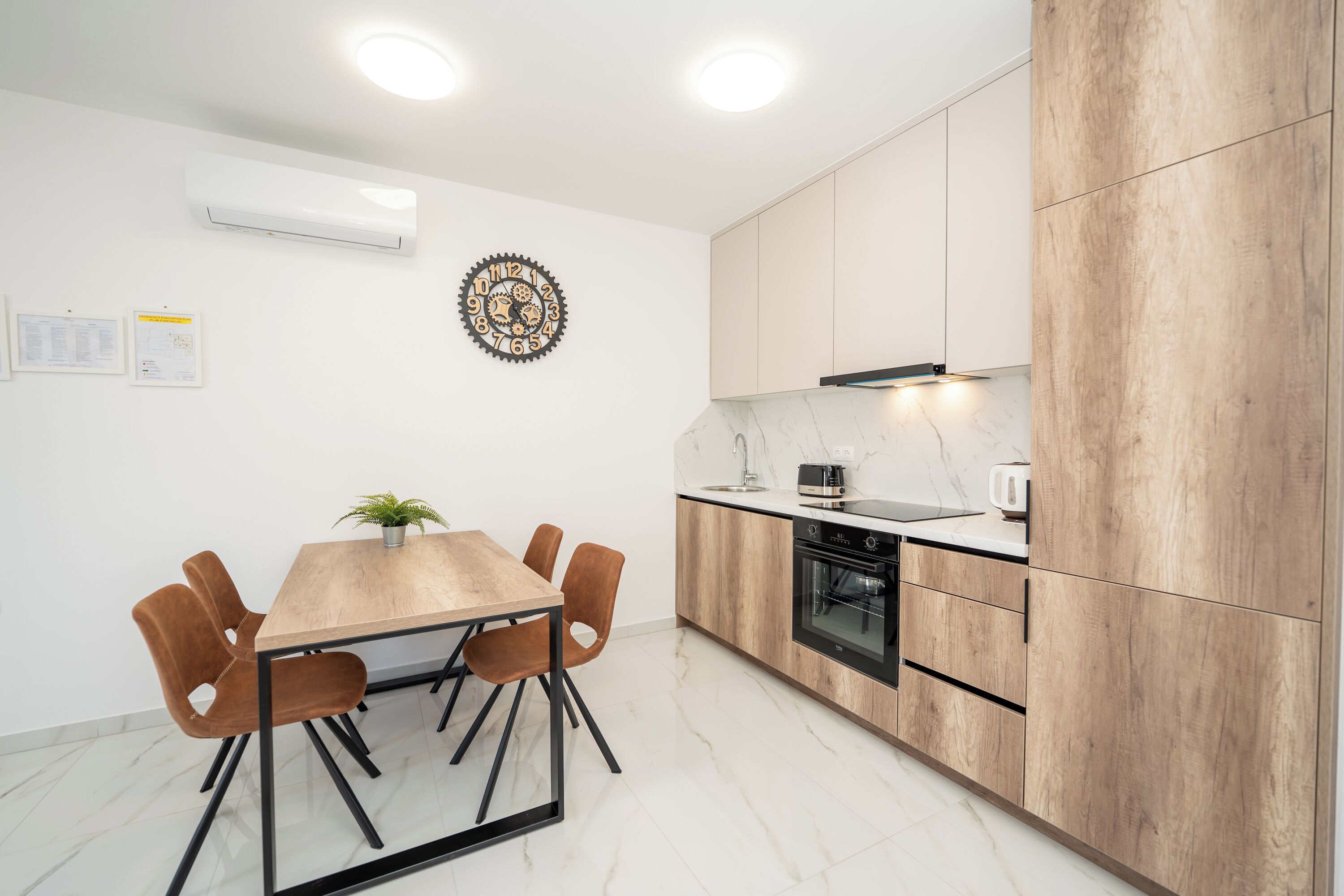 A modern kitchen with a wooden table and chairs, an oven, and a clock on the wall.