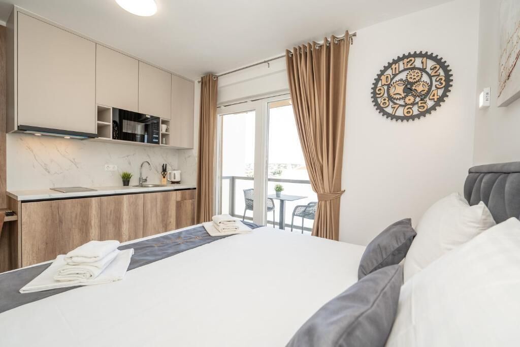 A hotel room with a bed, a small kitchenette, and a balcony with curtains.